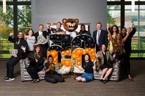 Oakland University Credit Union and Oakland University staff posing for a group photo around a lit up sign that says 65